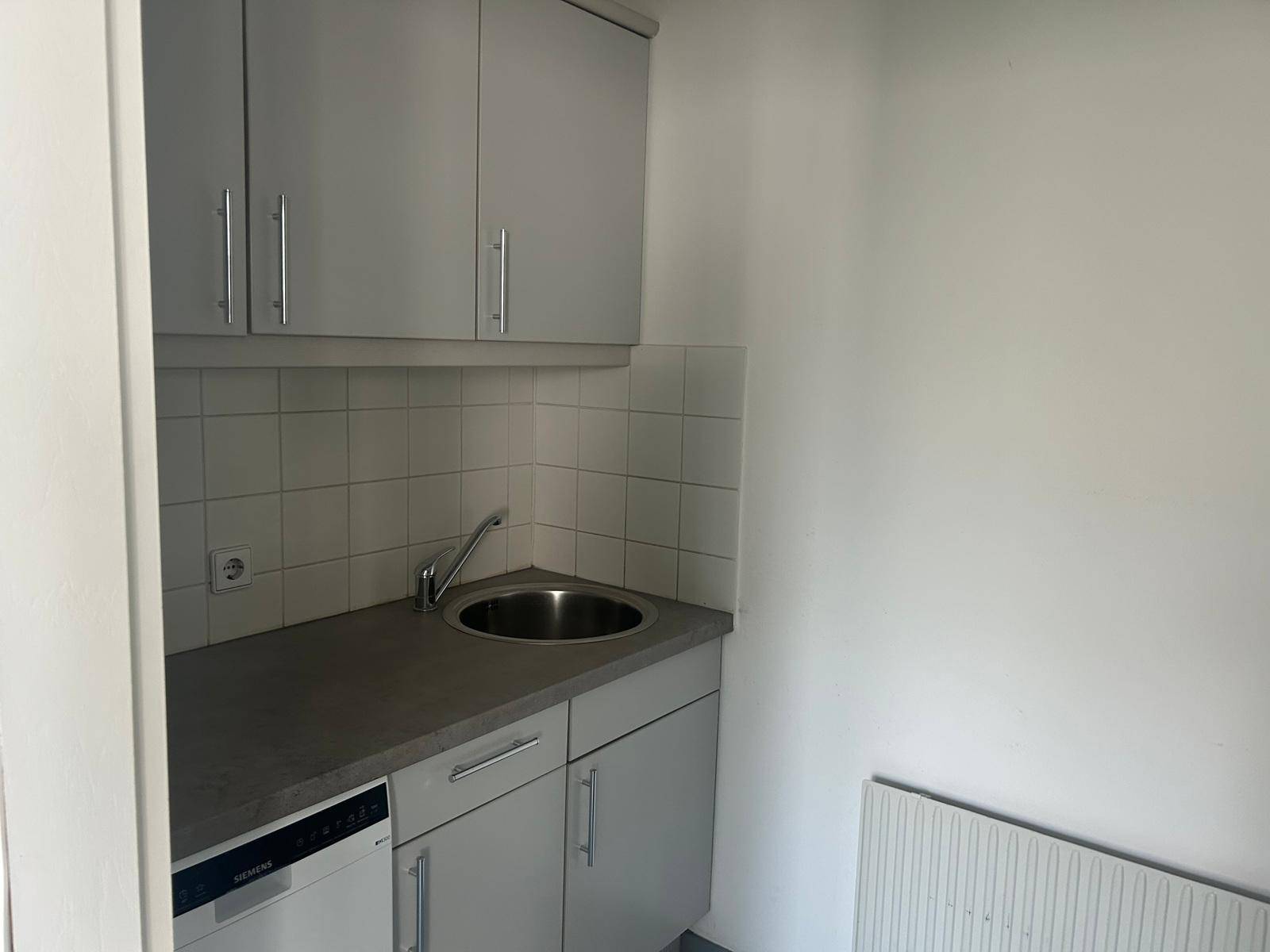 Kleine Küchenzeile mit grauen Schränken, Spülbecken und integriertem Geschirrspüler, ideal für Büroräume.