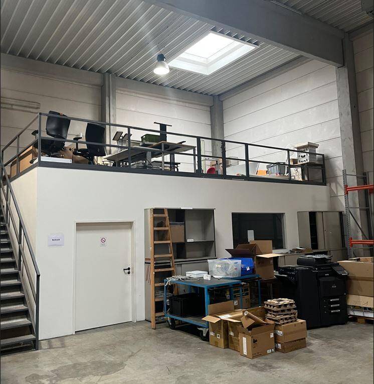 Lagerhalle mit einer erhöhten Bürofläche oder Mezzanine, Metalltreppe und Regalen.