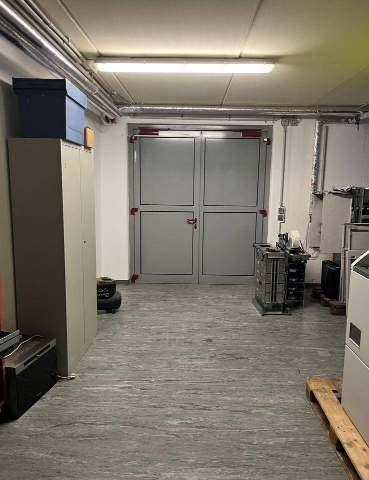 Lagerraum mit grauen Doppeltüren, Regalen und sichtbaren Rohren an der Decke.