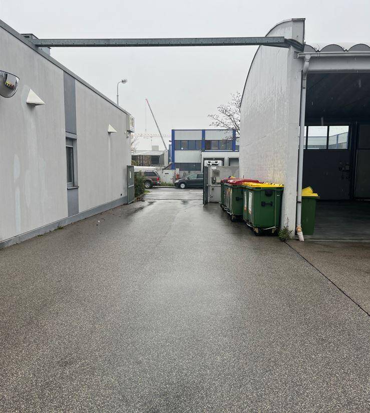Außenansicht eines Gewerbegebiets mit einem gepflasterten Weg zwischen zwei Gebäuden und Mülltonnen.