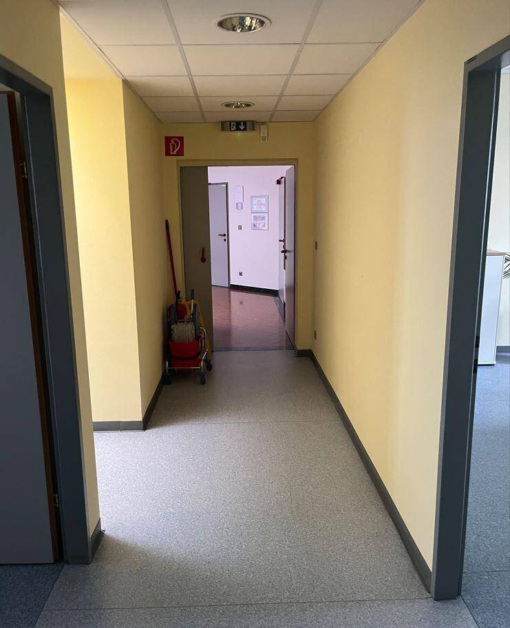Langer Flur mit hellgelben Wänden, grauem Boden und mehreren Türen, die zu Büros führen.