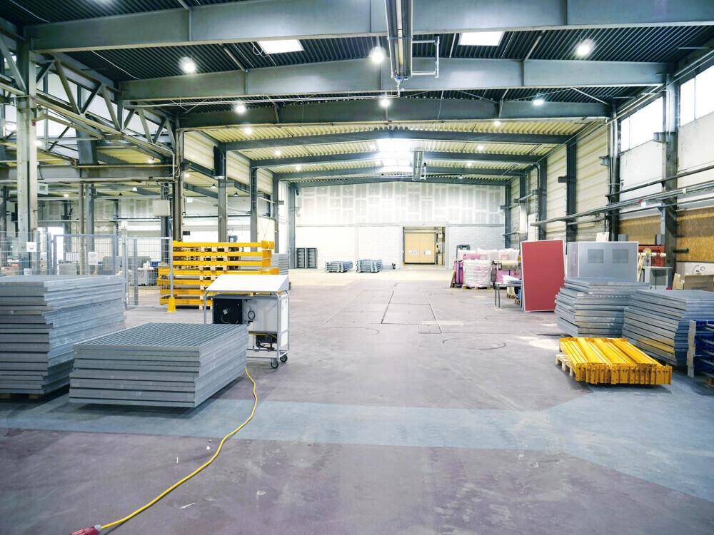Große Lagerhalle mit hohen Decken, Oberlichtern und verschiedenen gestapelten Materialien auf dem Industrieboden.