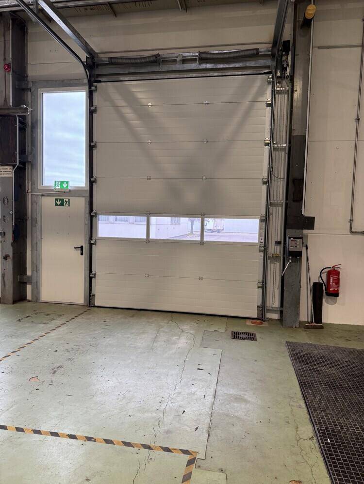 Großes Sektionaltor mit integrierter Tür und Fenstern in einer Industriehalle, daneben ein Feuerlöscher.