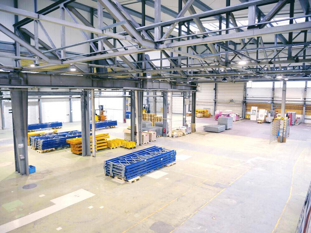 Geräumige Lagerhalle mit hoher Decke, sichtbaren Stahlträgern und gestapelten Materialien auf dem Betonboden.