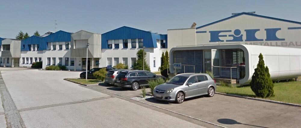 Modernes Bürogebäude mit blauen Dächern und einem Parkplatz davor an einem sonnigen Tag.