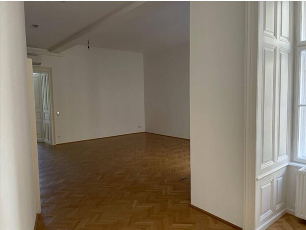 Großer Raum mit Fischgrätparkett, weißen Wänden und dekorativer Holzvertäfelung neben dem Fenster.