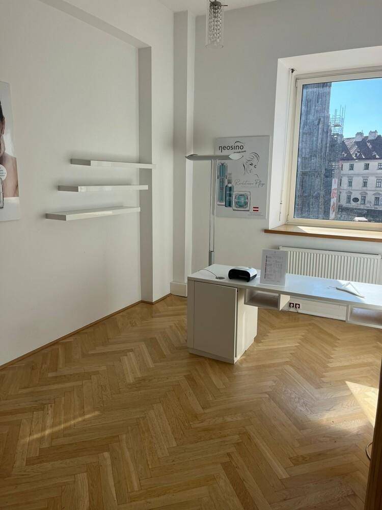 Heller Büroraum mit schwebenden Regalen und einem Schreibtisch, Fischgrätparkett und großem Fenster.