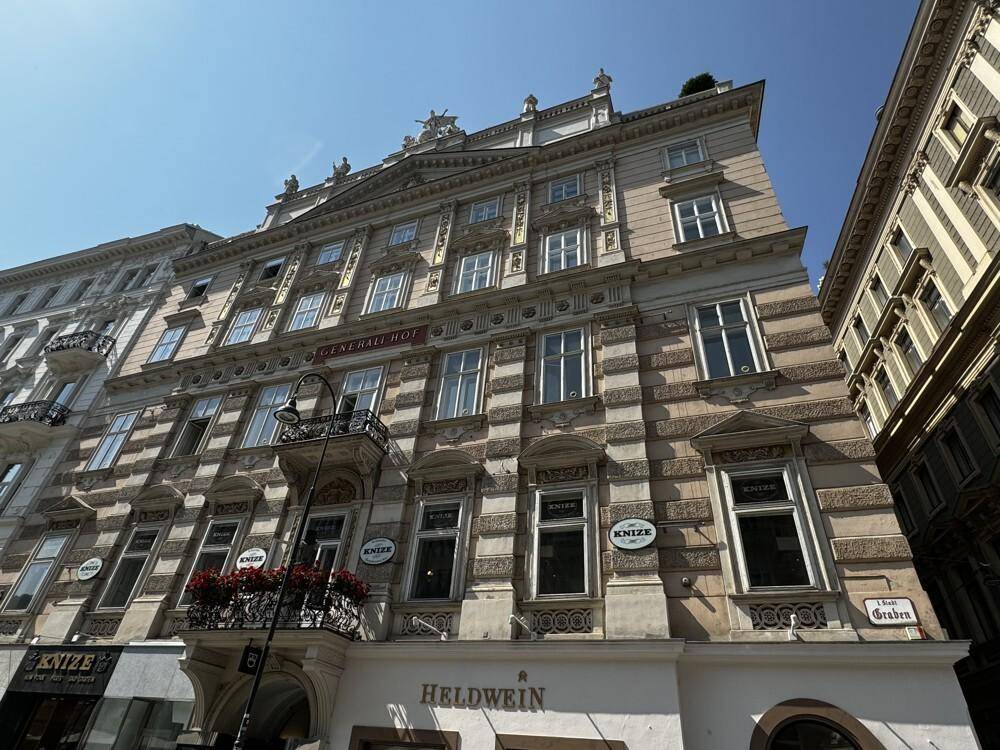 Historisches Gebäude mit reich verzierter Fassade und Blick auf die angrenzende Straße und weitere Gebäude.