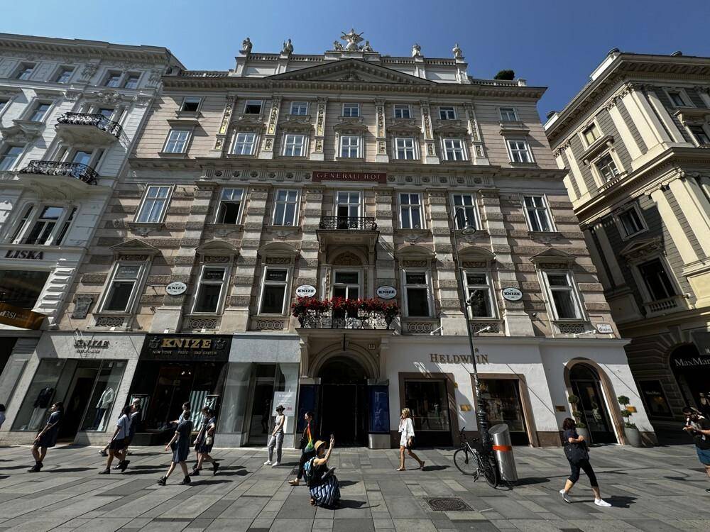 Die prächtige Fassade des historischen Gebäudes mit Geschäften und Passanten an einem sonnigen Tag.