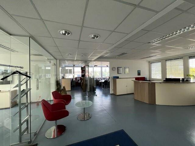 Helles und modernes Büro mit Empfangsbereich, roten Sesseln und Glasabtrennungen.