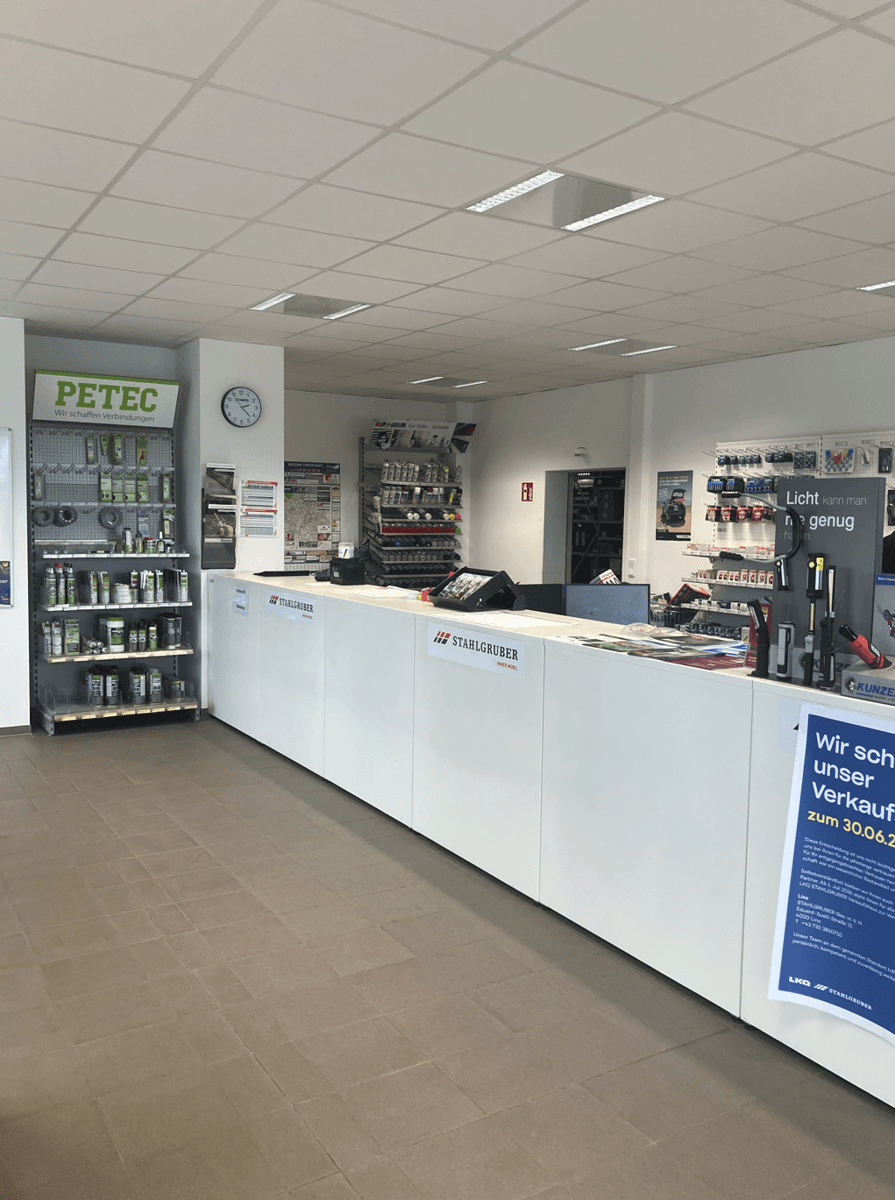 Heller Verkaufsraum mit einer langen weißen Theke und Regalen, die verschiedene Produkte für Kunden präsentieren.