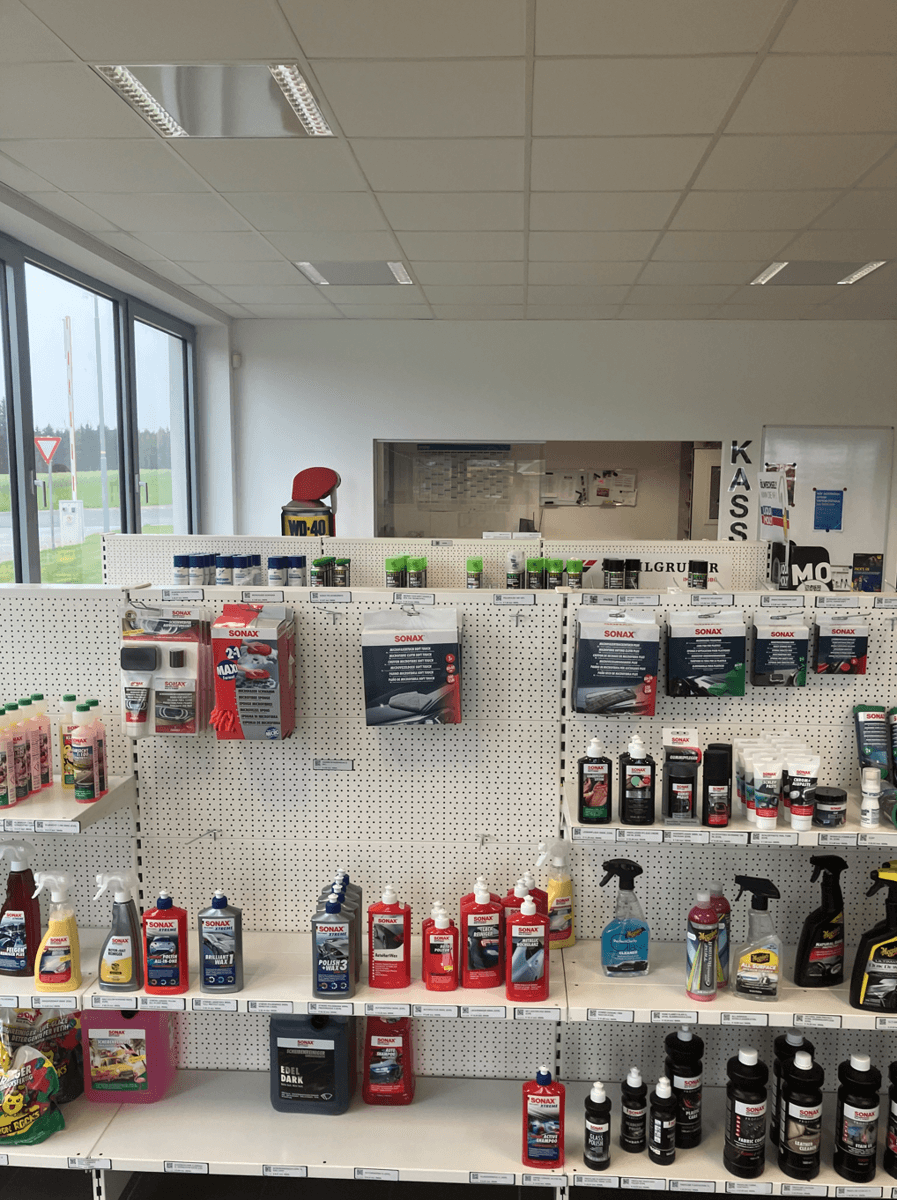 Produktpräsentation an einer weißen Lochwand mit einer Vielzahl von Autopflegeprodukten und großen Fenstern im Hintergrund.