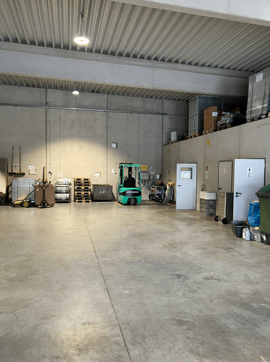 Lagerhalle mit Betonwänden, einem Gabelstapler und gestapelten Paletten, bereit für den Warentransport und die Lagerung.