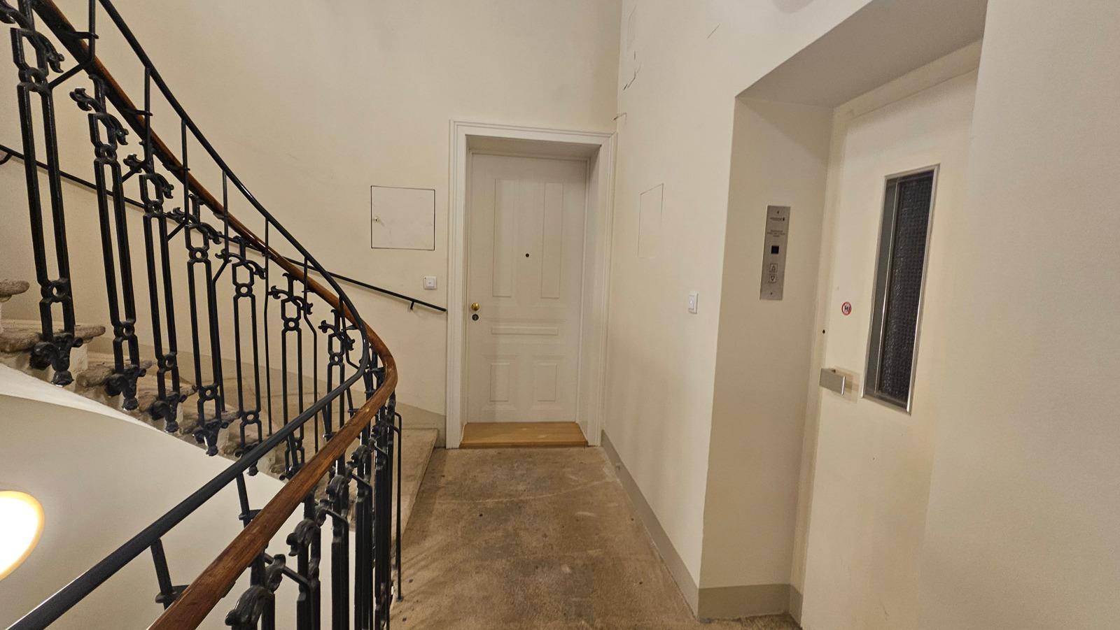 Heller Flur mit eleganter geschwungener Treppe und einem modernen Aufzug in einem Altbau.