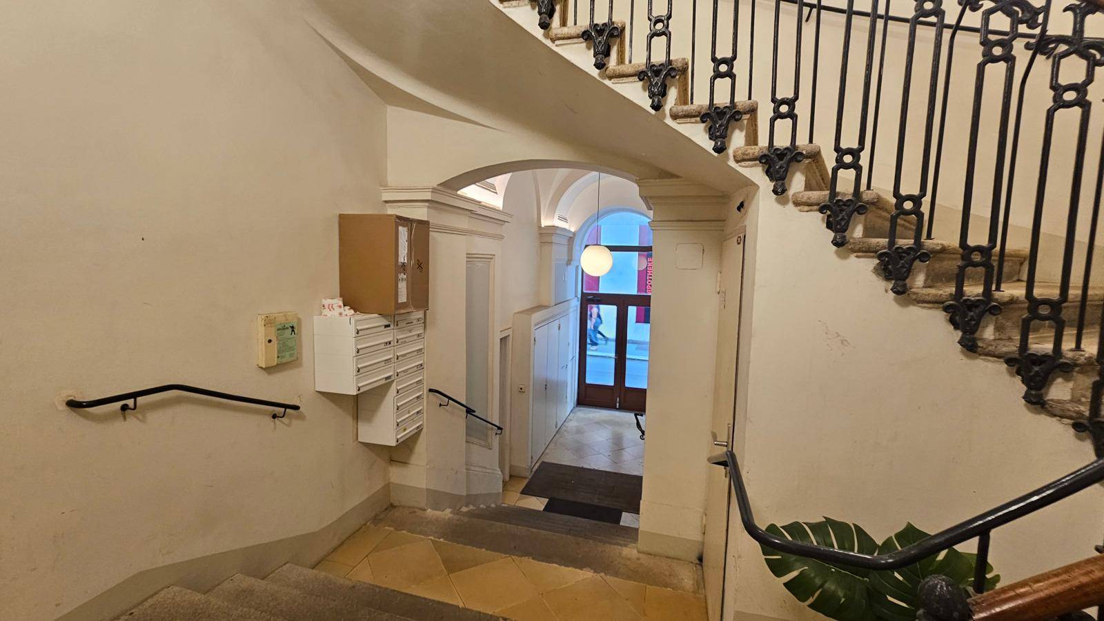 Historisches Treppenhaus mit geschwungener Treppe, Briefkästen und einem Bogen zum Gebäudeeingang.