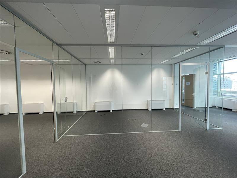 Großes Büro mit Teppichboden und modernen Glasabtrennungen für separate Arbeitsbereiche.