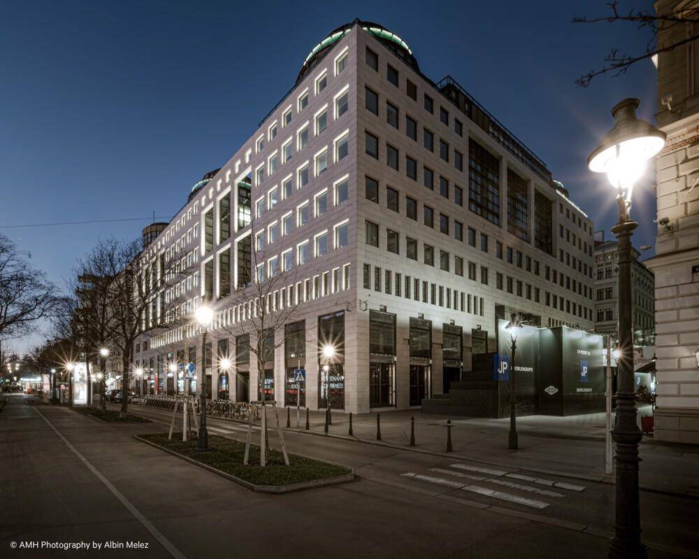 Ansicht des modernen Gebäudes von der Straße bei Nacht, mit beleuchteten Fenstern und Laternen.