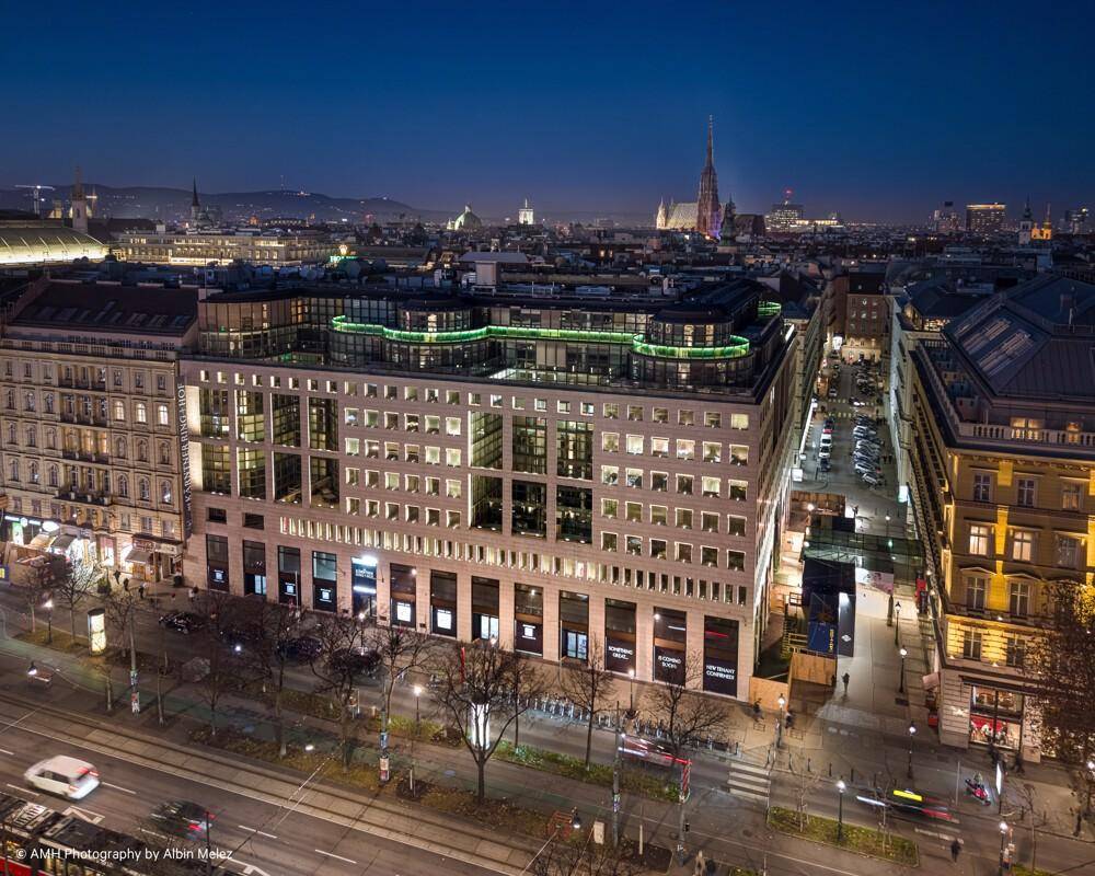 Luftaufnahme eines modernen Stadtgebäudes bei Nacht, umgeben von beleuchteten Straßen und historischen Strukturen.