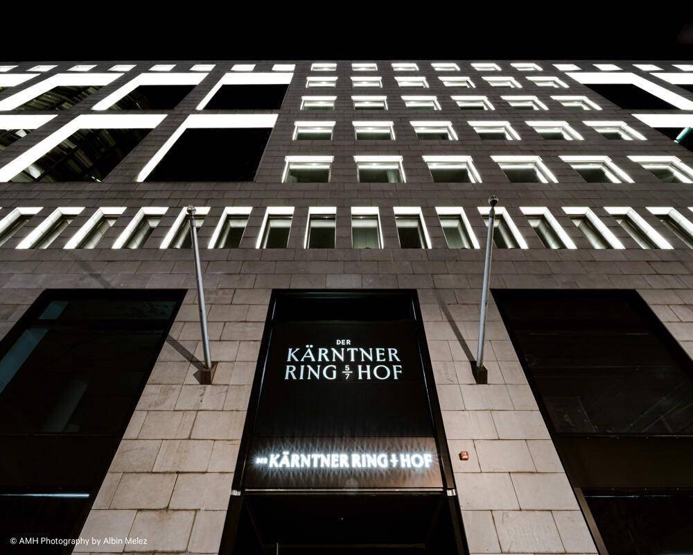 Nahaufnahme des Haupteingangs eines modernen Gebäudes mit markanter Beschilderung und vertikalen Fensterreihen.