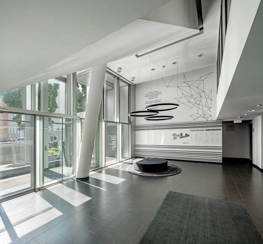 Geräumige, moderne Lobby mit hohen Decken, großen Fenstern und dunklem Fliesenboden.