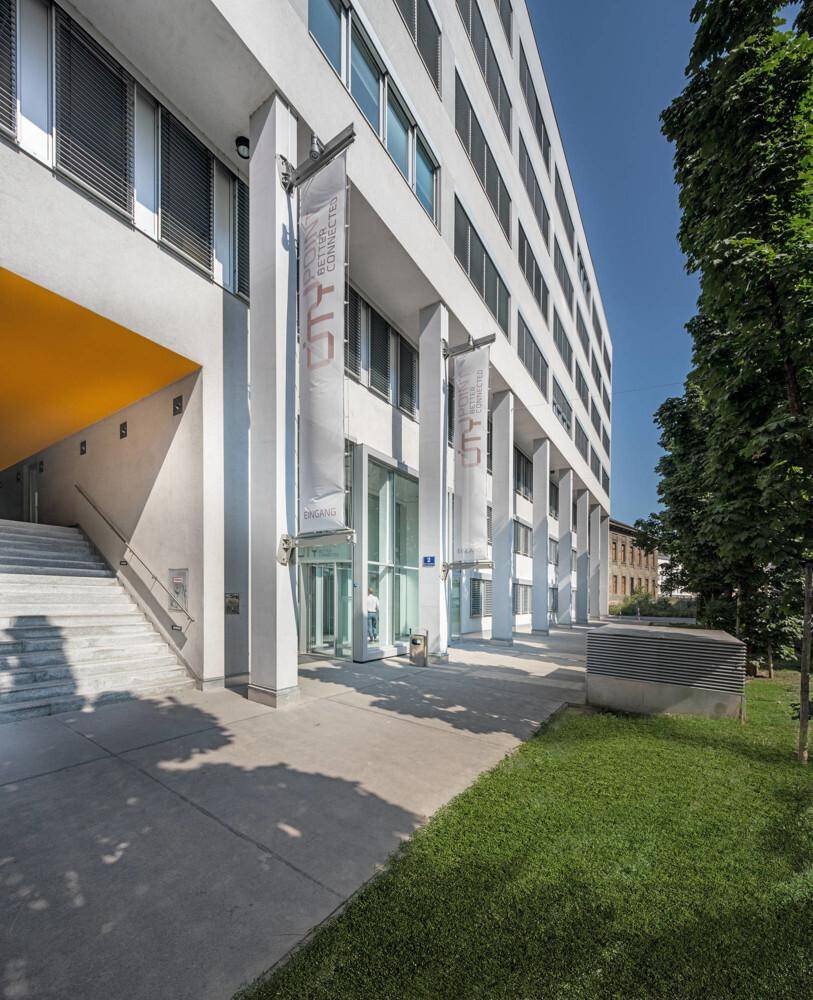 Moderne Bürogebäude-Fassade mit Säulen, großen Fenstern und einem grünen Rasenbereich.