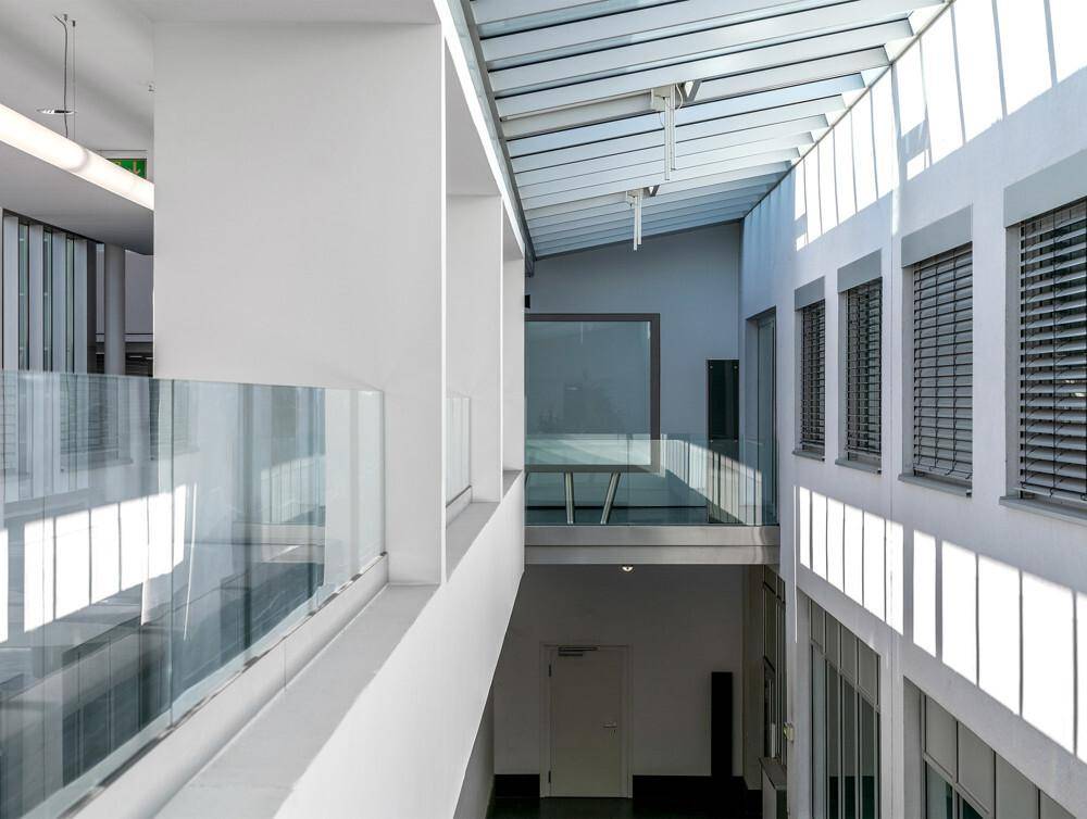 Heller Atriumbereich mit Glasgeländern, großen Fenstern und viel natürlichem Lichteinfall.