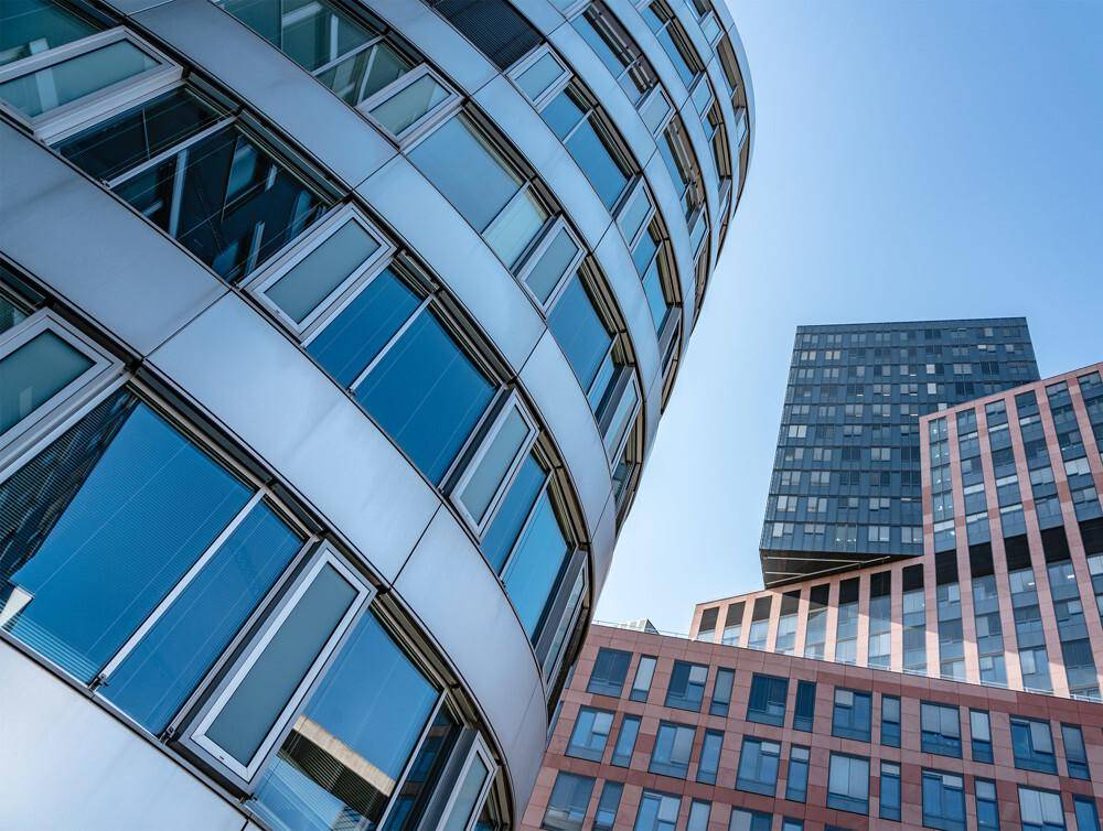 Architektonische Aufnahme von mehreren modernen Bürogebäuden mit Glasfassaden unter blauem Himmel.