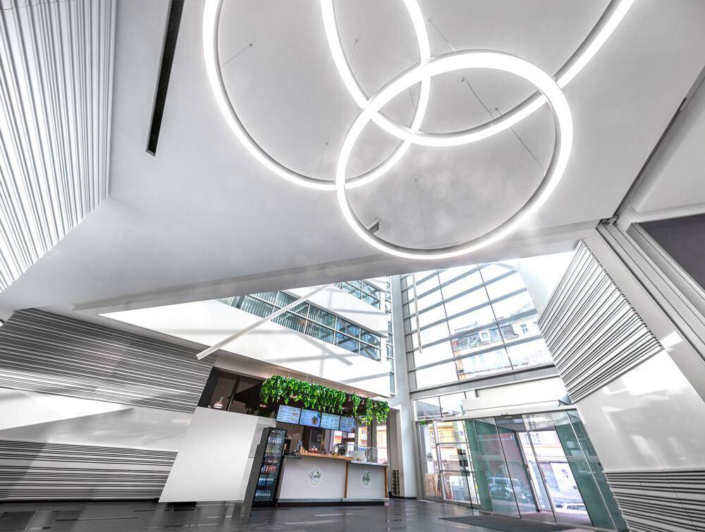 Helle, moderne Lobby mit hohen Decken, runden Leuchten und einem kleinen Café-Bereich.
