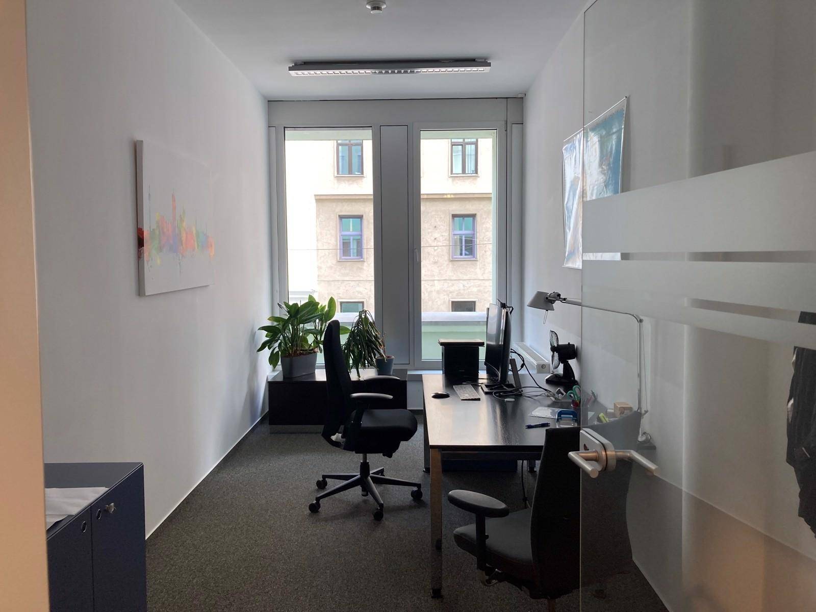 Modernes Einzelbüro mit Schreibtisch, Bürostühlen und Blick auf die umliegenden Gebäude.