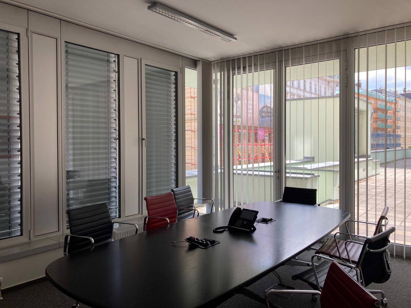 Konferenzraum mit großem Tisch, modernen Stühlen und Blick auf eine Dachterrasse.