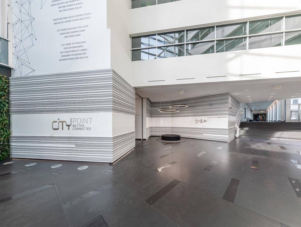 Weitläufige, moderne Lobby mit strukturierten Wänden, hohen Decken und minimalistischer Einrichtung.