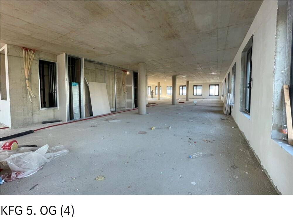 Großer, unfertiger Büroraum im Rohbauzustand mit Betonboden und vielen Fenstern.