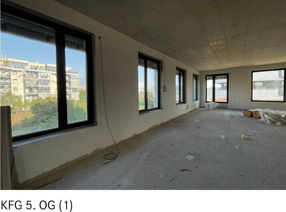 Unfertiger Büroraum mit großen Fenstern, die einen Blick auf die umliegende Stadt und Grünflächen bieten.
