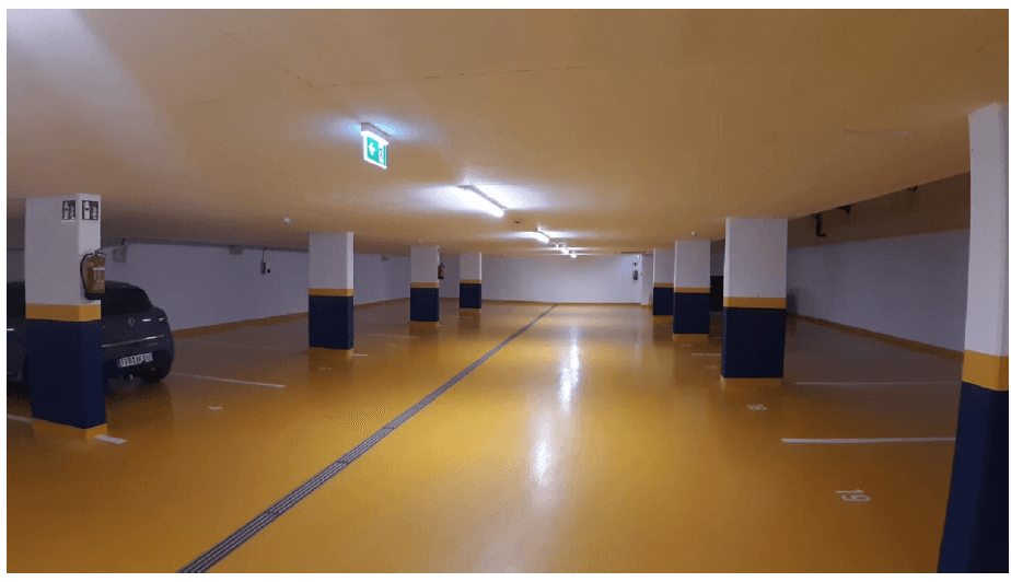 Saubere und gut beleuchtete Tiefgarage mit markierten Parkplätzen und gelbem Boden.
