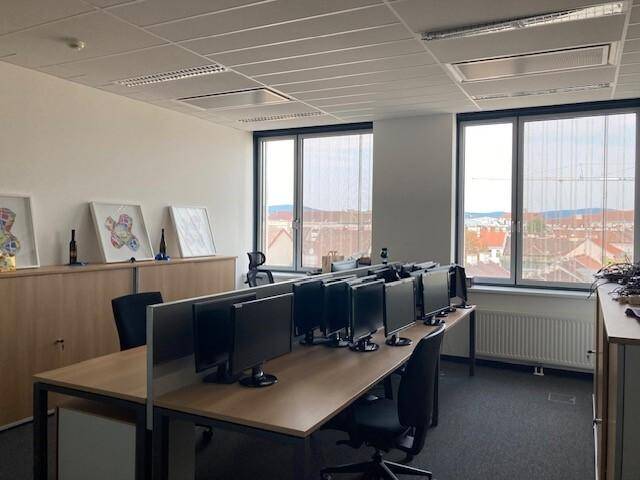 Großraumbüro mit vielen Computerarbeitsplätzen, Holzschränken und weitem Stadtblick.