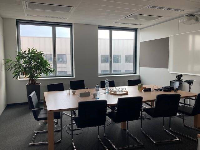 Besprechungsraum mit großem Konferenztisch, Stühlen und Projektionsfläche an der Wand.
