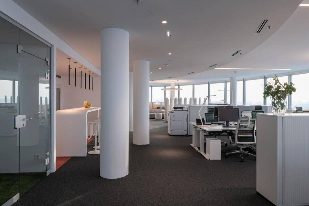 Großes offenes Büro mit vielen Arbeitsplätzen, Säulen und moderner Beleuchtung.