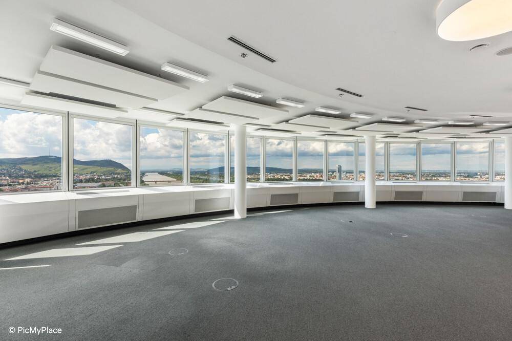 Geräumiger, leerer Büroraum mit Panoramablick, Teppichboden und moderner Deckenbeleuchtung.