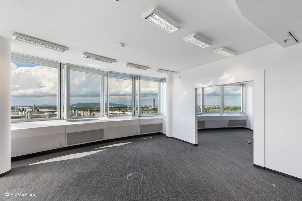 Heller, leerer Büroraum mit großen Fenstern, Teppichboden und weitem Stadtblick.