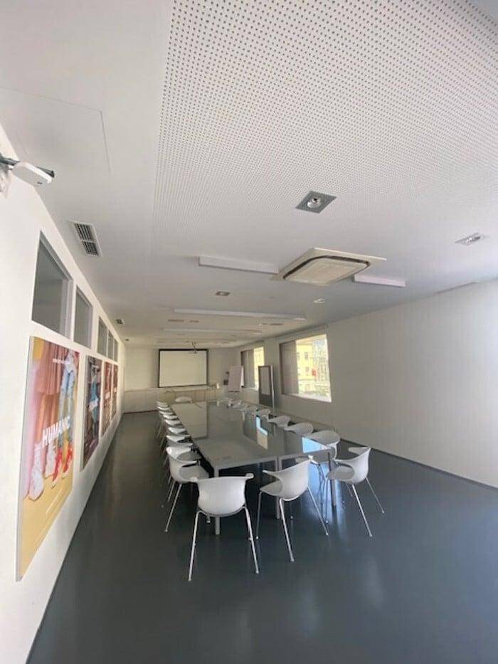 Geräumiger Konferenzraum mit langem Tisch, vielen Stühlen und einem Projektionsbildschirm.