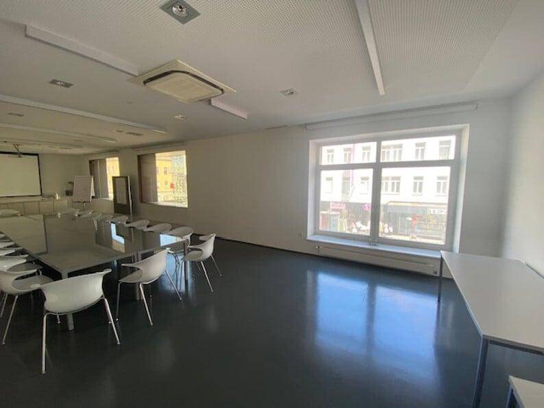 Heller Konferenzraum mit großem Fenster, langem Tisch und modernen Stühlen.