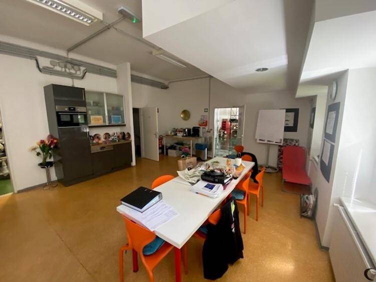 Helle Büroküche oder Pausenraum mit langer Tafel, orangefarbenen Stühlen und Einbauküche.