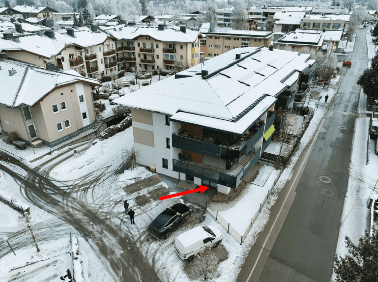 Luftaufnahme eines schneebedeckten Gebäudes mit Balkonen und umliegenden Häusern im Winter.