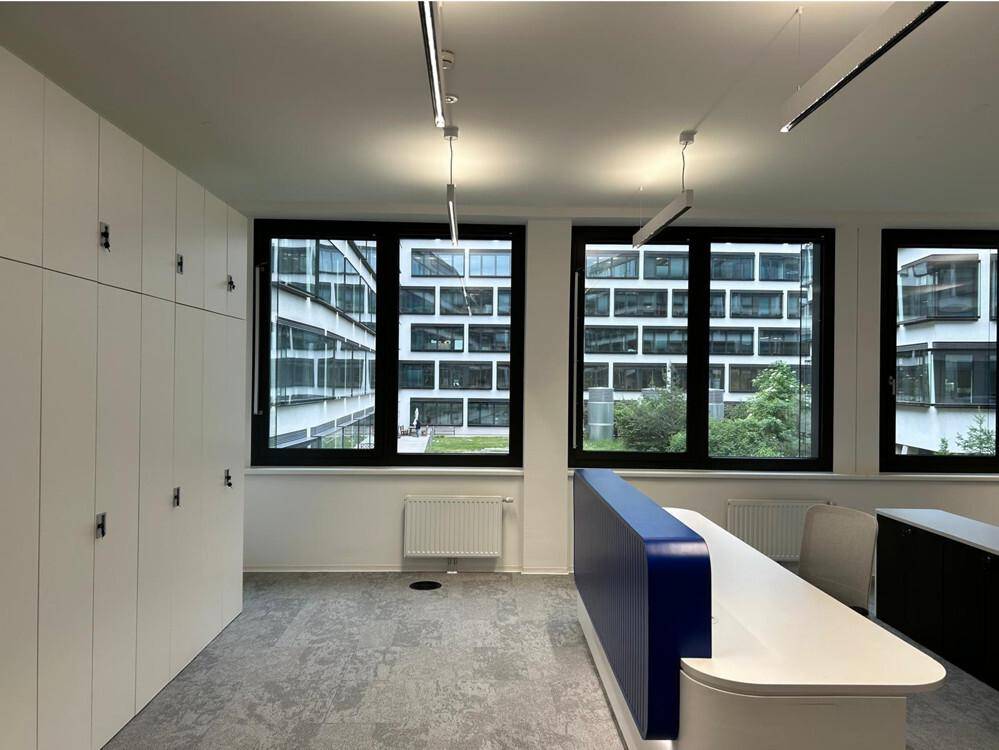 Moderner Bürobereich mit Schließfächern, großen Fenstern und Blick auf die umliegenden Gebäude im Innenhof.