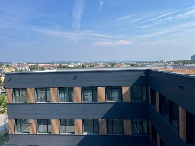 Oberer Teil eines modernen Gebäudes mit Fenstern und Holzdetails, bietet einen weiten Blick in die Ferne.