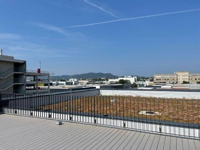 Dachterrassenblick über eine begrünte Dachfläche, mit städtischer Bebauung und Bergen im Hintergrund.