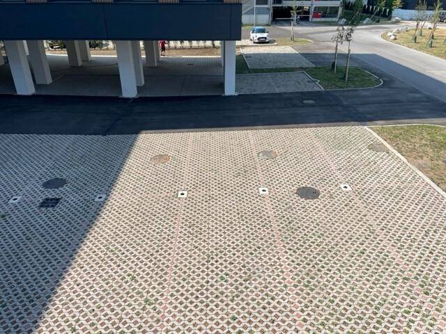 Außenparkplatz mit Rasengittersteinen, teilweise überdacht durch einen Gebäudevorsprung mit Säulen.