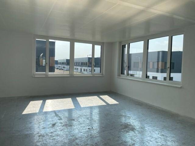 Heller, leerer Büroraum mit großen Fenstern, Betonboden und viel natürlichem Tageslicht.