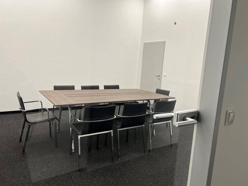 Besprechungsraum mit großem Holztisch, schwarzen Stühlen und dunklem Teppichboden.