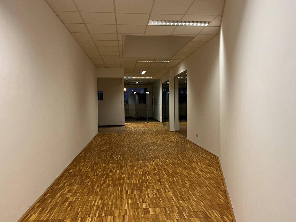 Langer Flur mit hellem Parkettboden und weißen Wänden, der zu weiteren Büroräumen führt.
